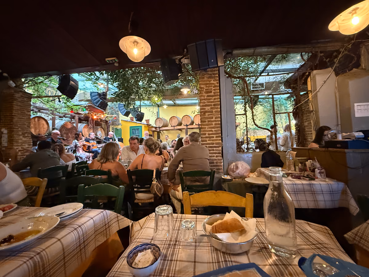 A busy taverna under hanging lamps, bread and water on a checked tablecloth